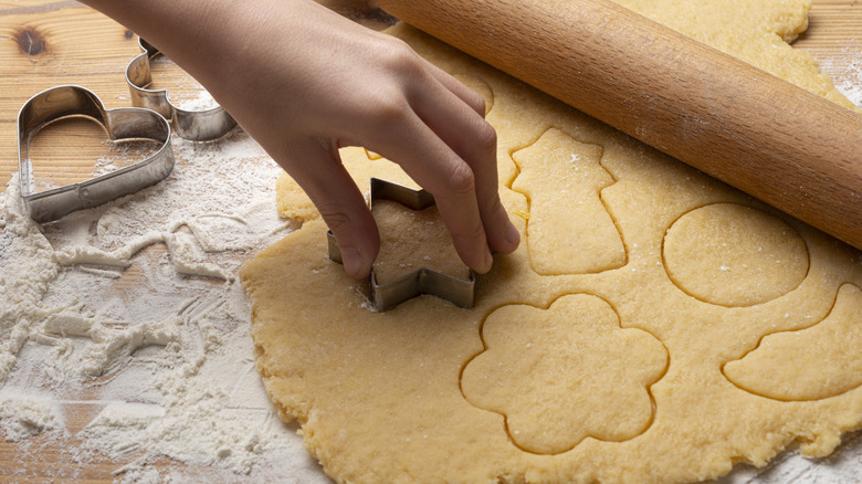 a person cuts out circle shapes from a sheet of sugar cookie dough