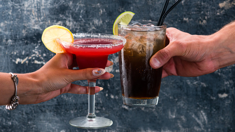 a man and woman cheersing a margarita and cola
