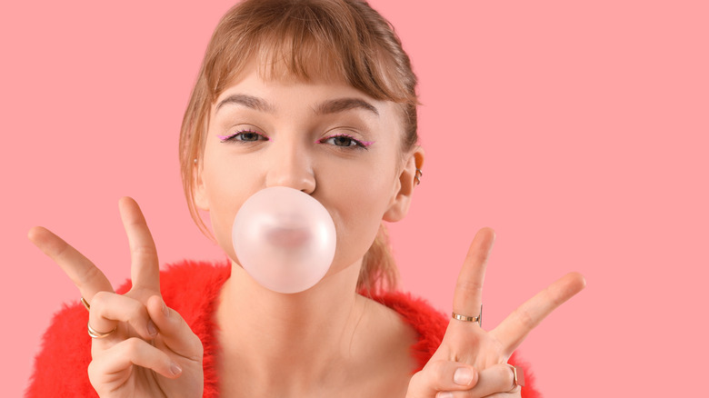 A young woman blowing a bubble and holding up peace signs with both hands