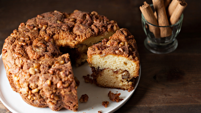 A round coffee cake with cinnamon sticks on a dark background.