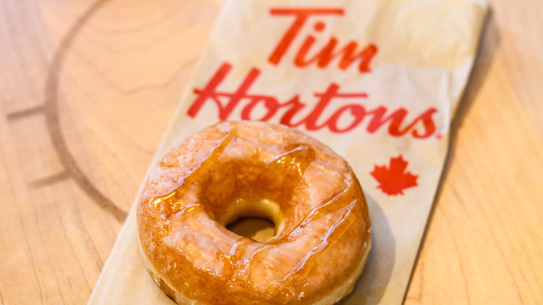 A Tim Hortons donut on top of a branded brown paper bag.