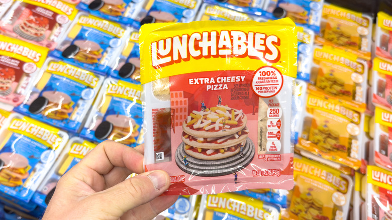 A hand holding a Pizza Lunchables over various different flavors