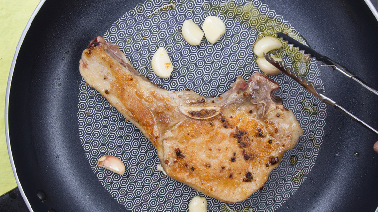 cooking pork chop in a pan with garlic cloves and oil