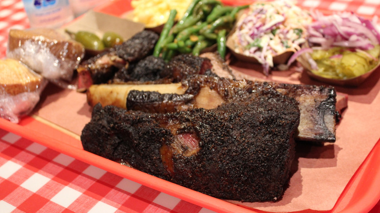 Dino ribs from Terry Black's Barbecue in Lockhart, Texas on a tray surrounded by sides in the background