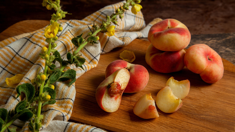 Donut peaches, some whole and some sliced on a cutting board