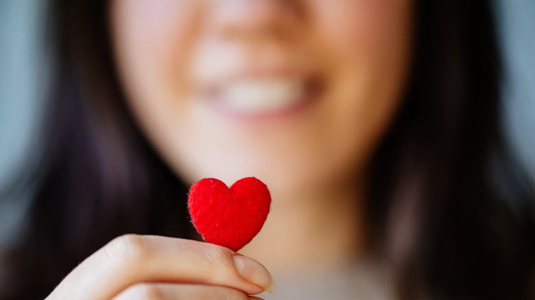 A women holding a small pink heart and smiling in the background