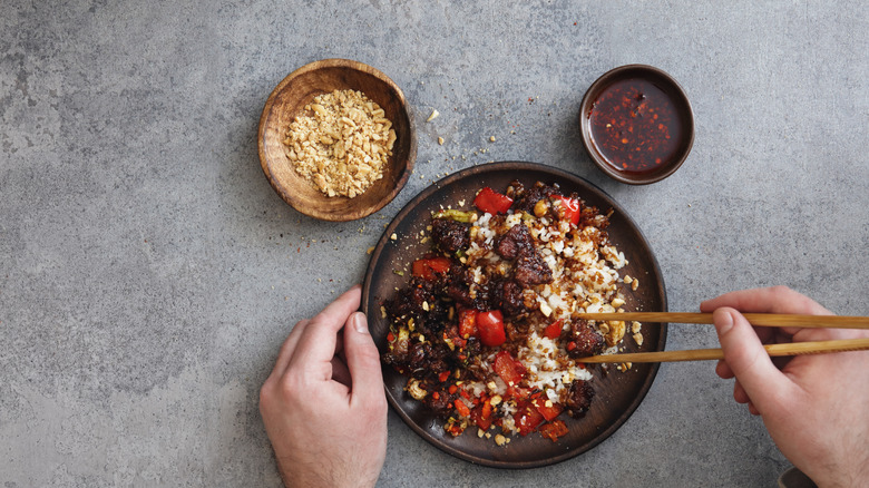 A man eats a dish with chopsticks, with Sichuan peppercorns and chili oil on the side