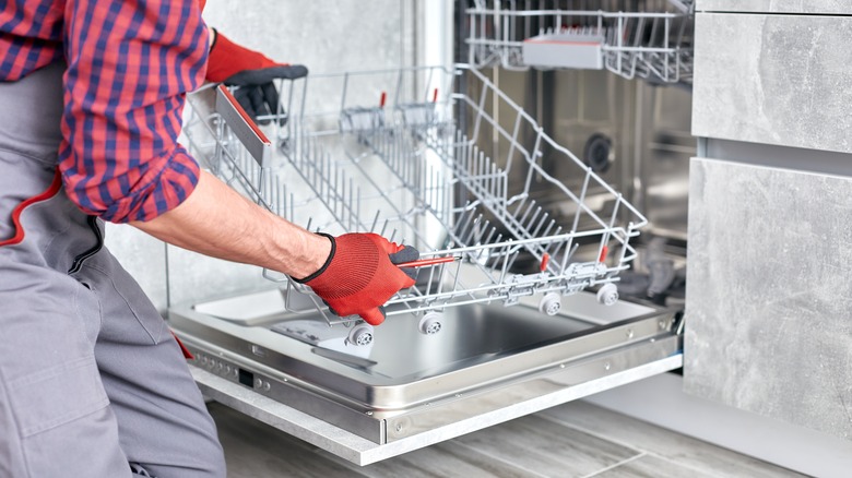 Workman placing bottom rack in dishwasher