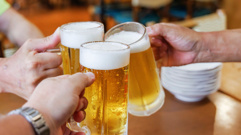Three hands clinking beer mugs over a table