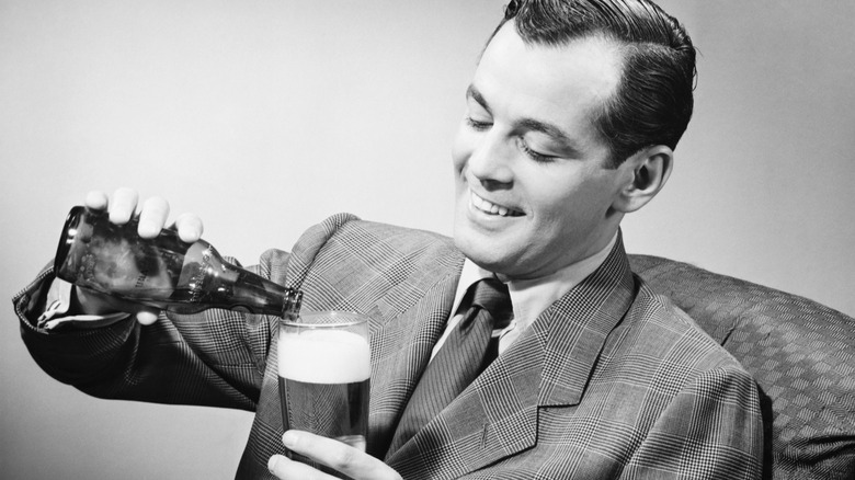 An old-fashioned black and white image of a man in a business suit pouring a beer into a glass from an amber bottle