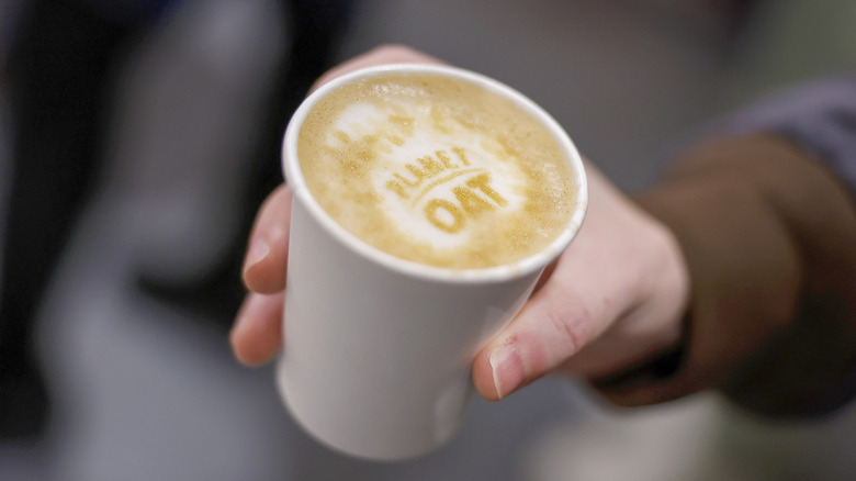 Customer holds a cup of coffee with "Planet Oat" written in latte art