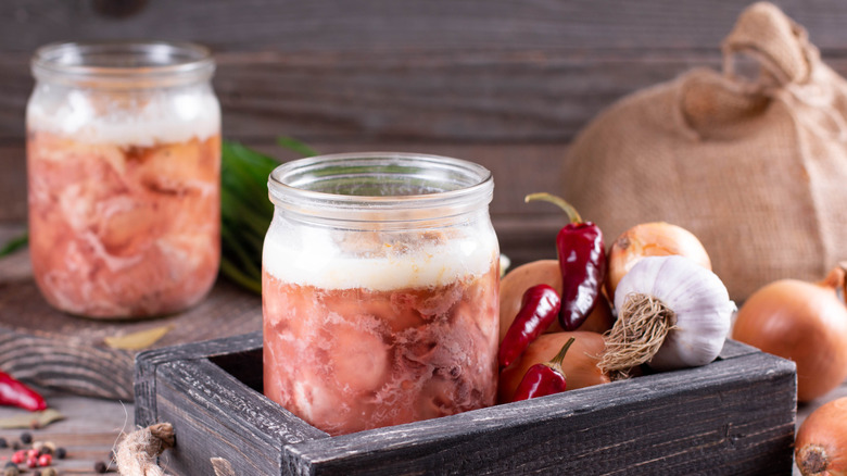 Jars of pork submerged in liquid, with fresh garlic and chilis beside them
