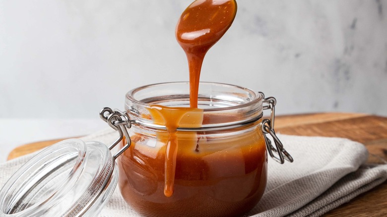 a glass jar of caramel with a spoon of caramel above it