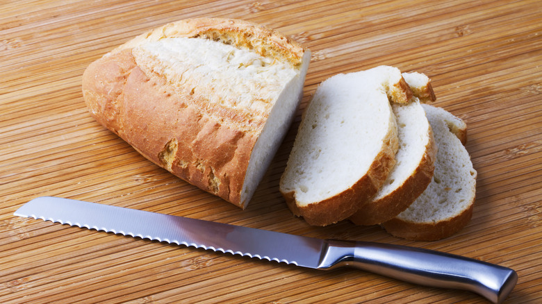 Serrated knife on wooden table with a loaf of freshly sliced bread