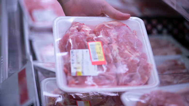 Refrigerated packaged chicken with label in the hand of a shopper