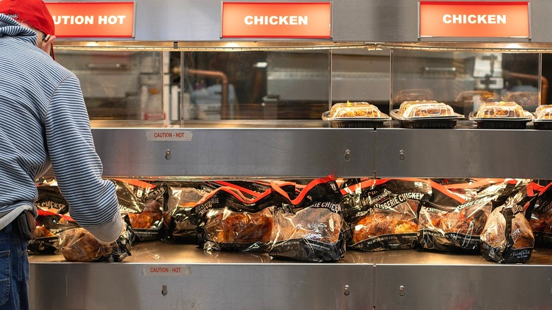 A man in a red baseball cap selecting a bagged rotisserie chicken at Costco