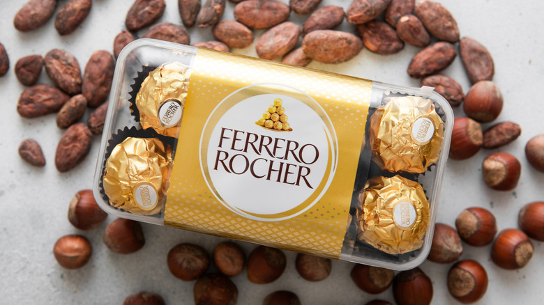 a package of Ferrero Rocher on top of a mound of hazelnuts and cocoa beans