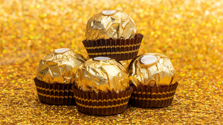 a stack of four Ferrero Rocher candies in gold wrapping on a glittery gold background