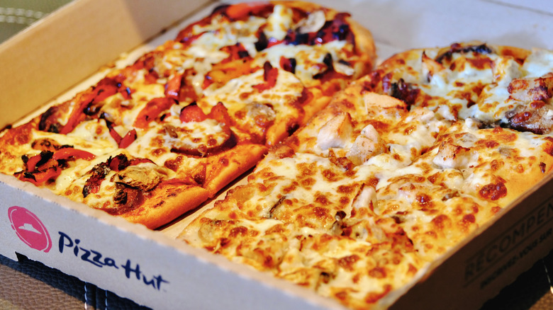 Two different kinds of freshly-made pizzas from pizza hut inside of an open box.