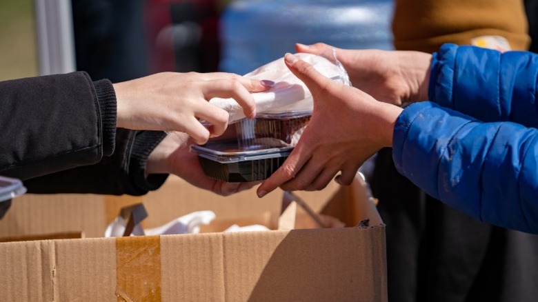 A person giving wrapped up donated food to another person out of a cardboard box.