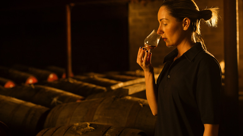 Person nosing whiskey among barrels
