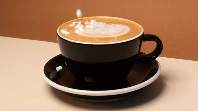Cafe latté in a black mug on a black saucer being garnished with tiny marshmallows from Vesta Coffee Roasters