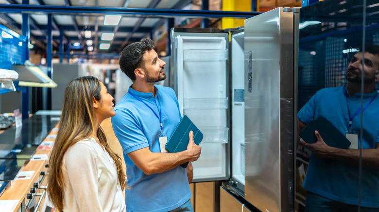 A sales associate showing a refrigerator to a customer.