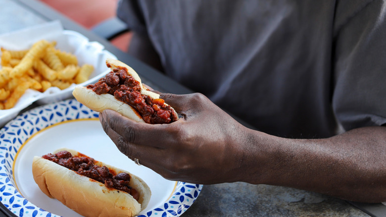 Man eating two hot dogs covered in meat sauce with a side of fries