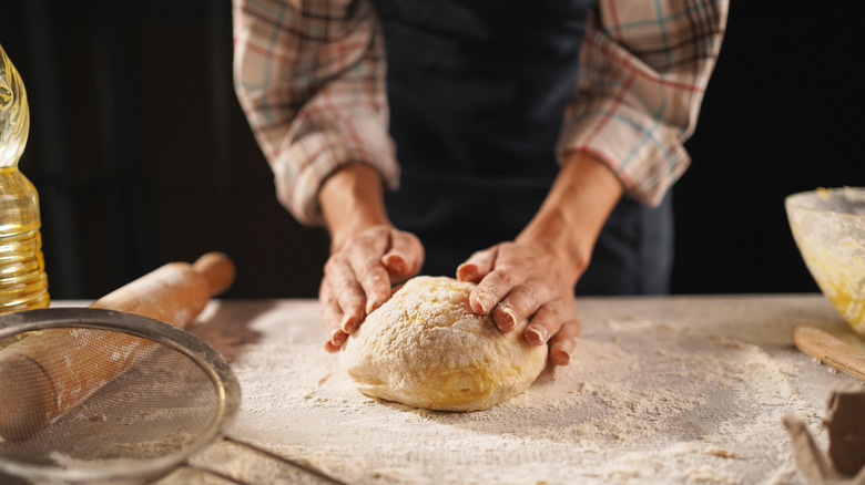 A professional artisan baker kneading a loaf of dough.