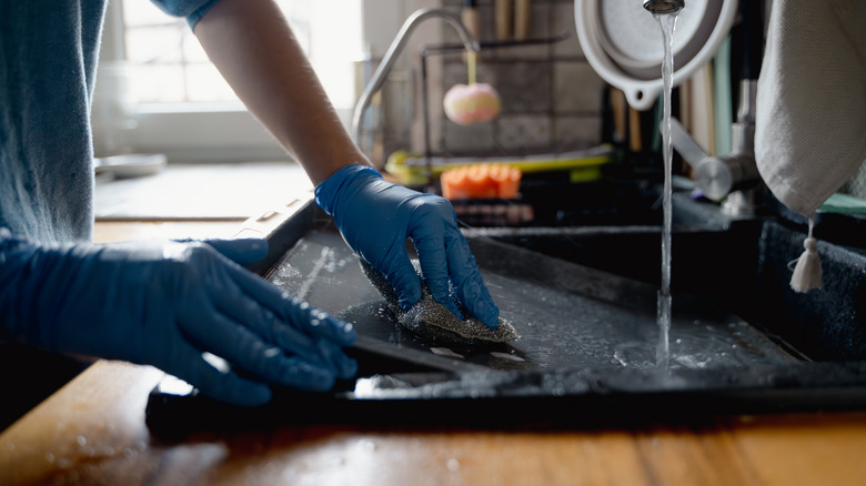 Gloved hands wash baking tray in the sink