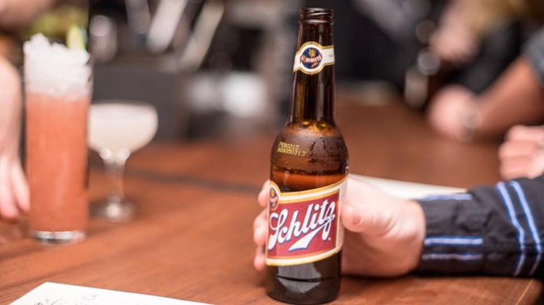 Man holding bottle of Schlitz beer on table