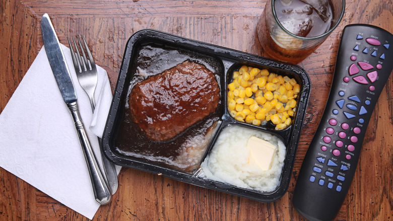 Dinner in plastic serving tray with salisbury steak, corn, and mashed potatoes, next to a remote
