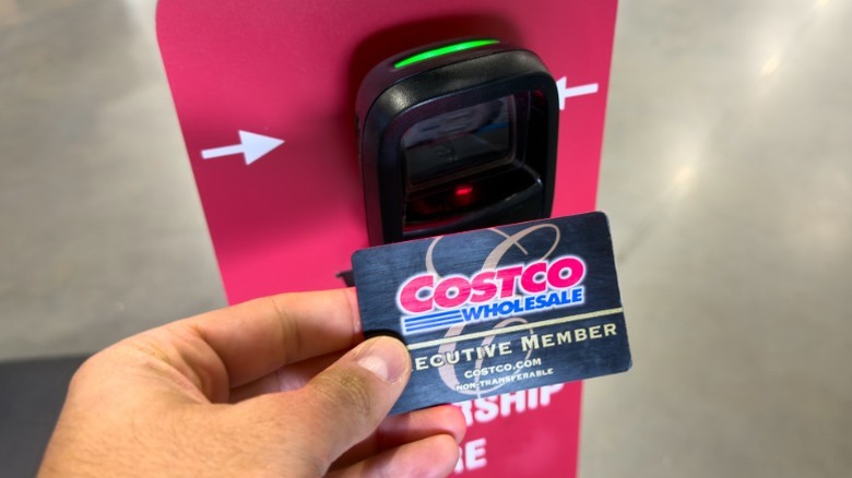 A person's hand holding a Costco Executive member card up to a typical store entrance scanner.