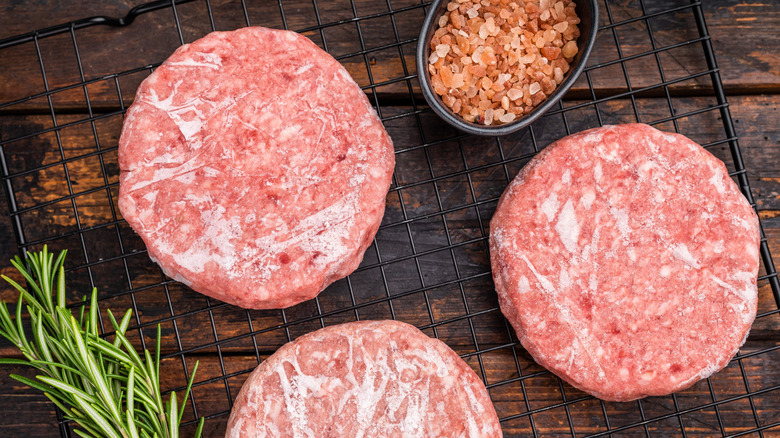 Three burger patties with seasonings ready for grilling.