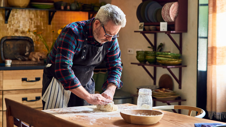 A man leans over a table as he kneads dough.
