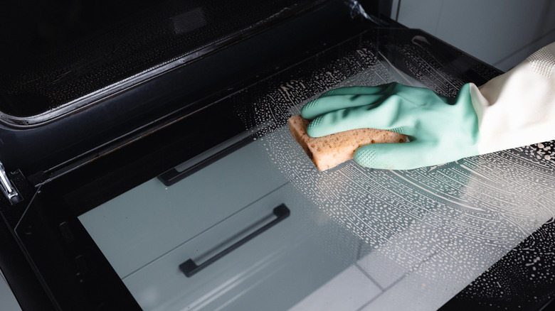 An individual cleaning an oven door.