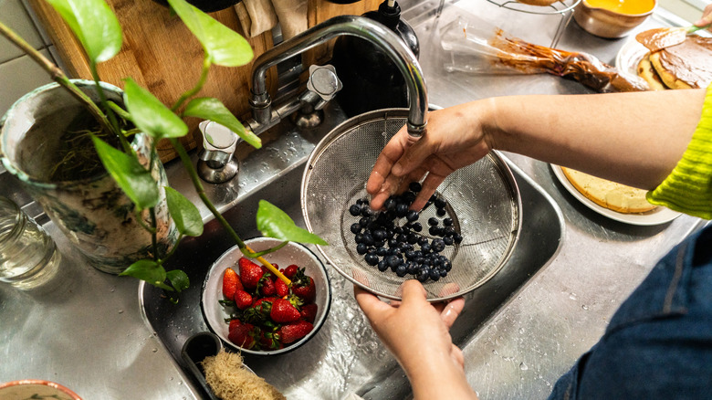 A person washing berries on the sink using a strainer