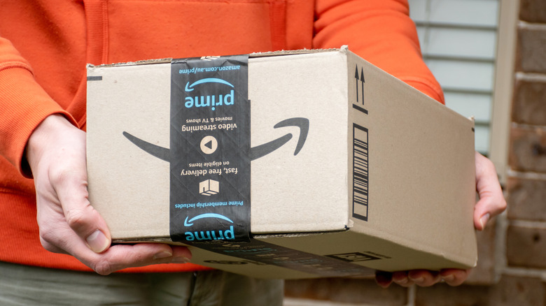 A person in an orange sweater holding an Amazon delivery box.