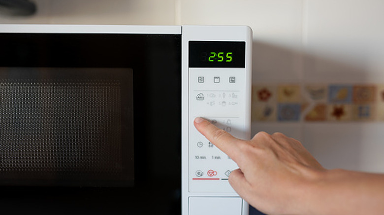 Person's finger pressing a setting button on a microwave