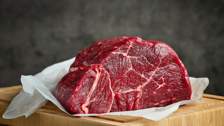 A huge chunk of raw meat placed on wooden tray