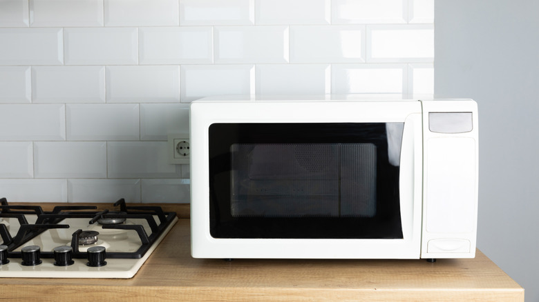 A white microwave on a countertop, next to a stove