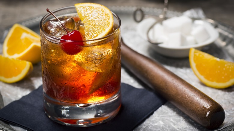 A whiskey cocktail with a cherry and orange slice
