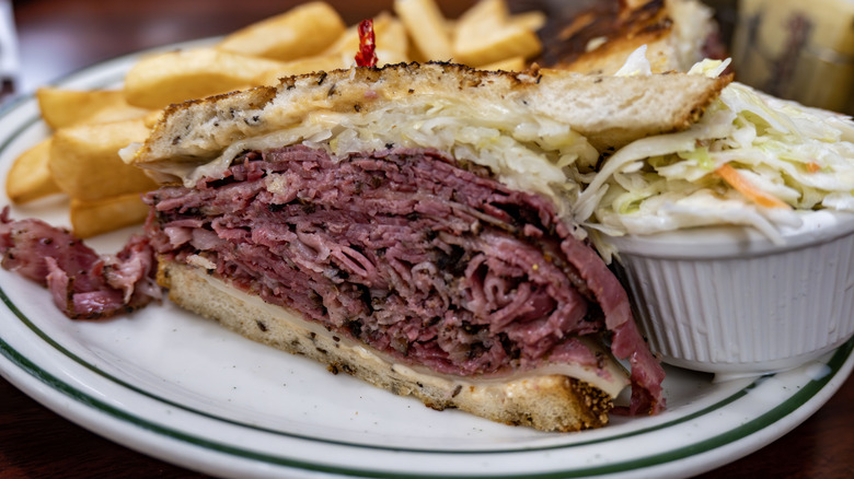 Half sandwich of smoked pastrami with french fries and coleslaw on plate.