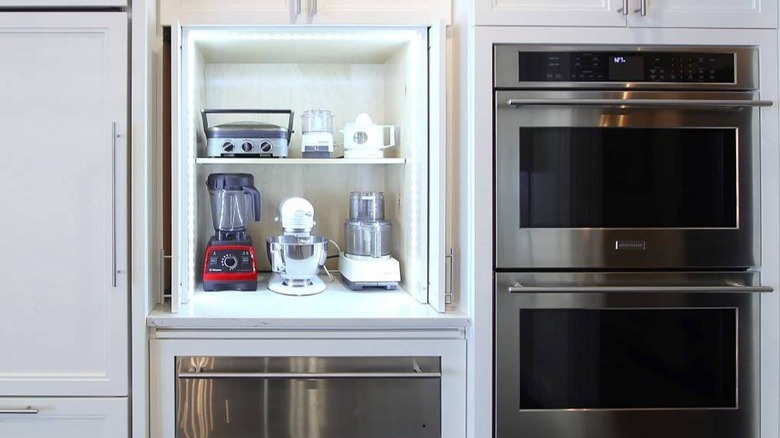 Shelving unit holding a blender, mixer, food processor, and other kitchen appliances