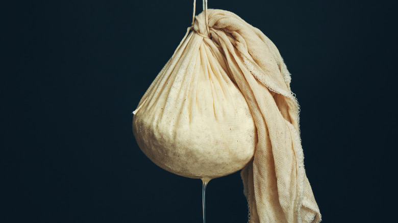 Bag of beige cheesecloth hanging up to let homemade cheese drain