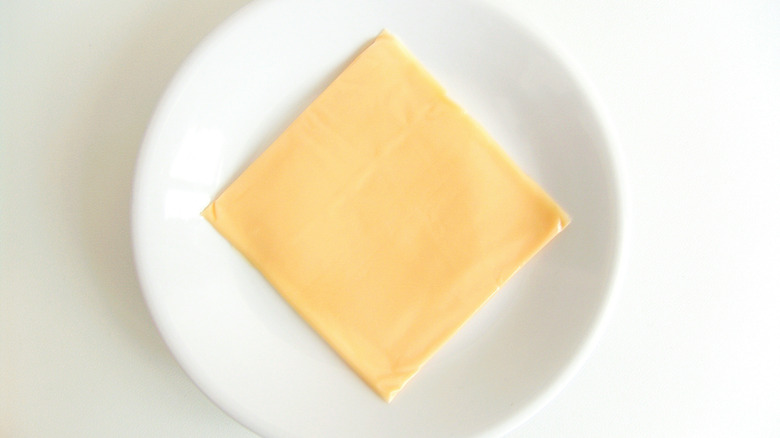 One slice of American cheese on a white plate on a white background