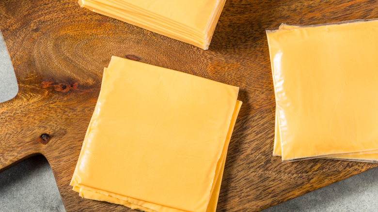 Three piles of individually wrapped slices of American cheese on a wooden board