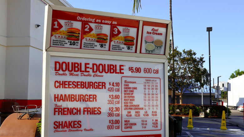 The menu at the drive-thru at an In-N-Out Burger in sunny Los Angeles, California lists burgers, fries, shakes, and drinks in bold red text, along with pricing and nutritional info.