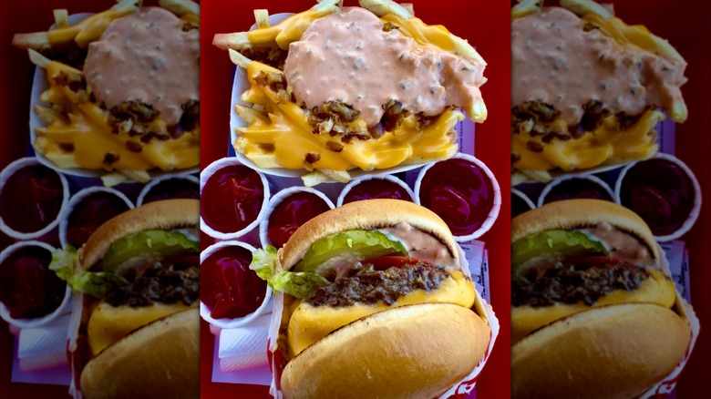 A Double-Double cheeseburger and French fries from In-N-Out, both served Animal Style﻿, sit beside five small cups of ketchup on a serving tray.