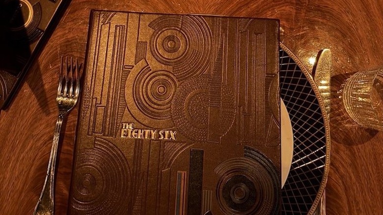 A closed menu from The Eighty Six in New York City sitting atop a plate next to silverware.